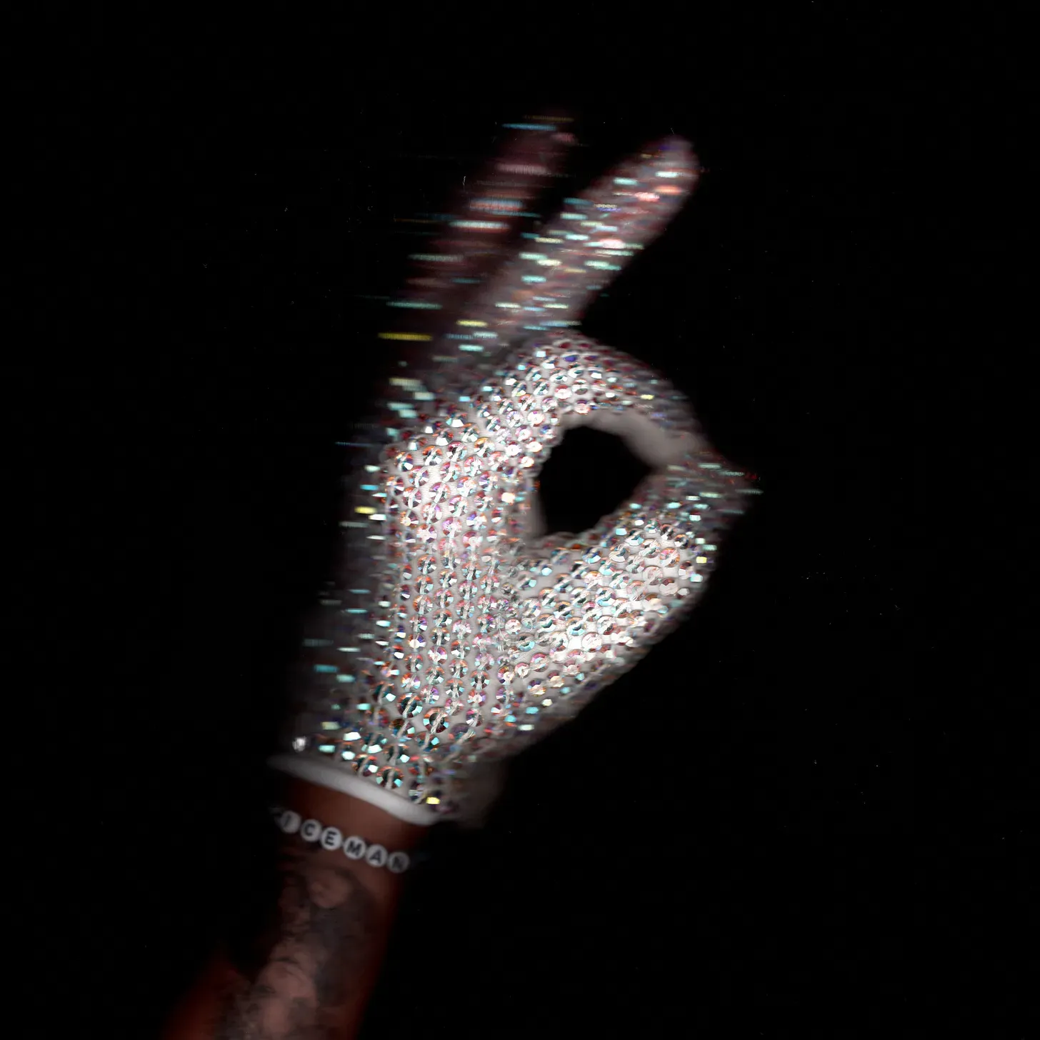 Crystal rhinestone glove on a hand making an OK gesture against a black background