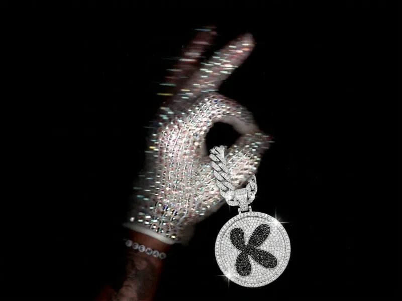 Round fully rhinestone-encrusted keychain with a rhinestone brand logo and a thick diamond chain threaded through the thumb of a sparkling crystal-gloved hand, white background, luxury product edit