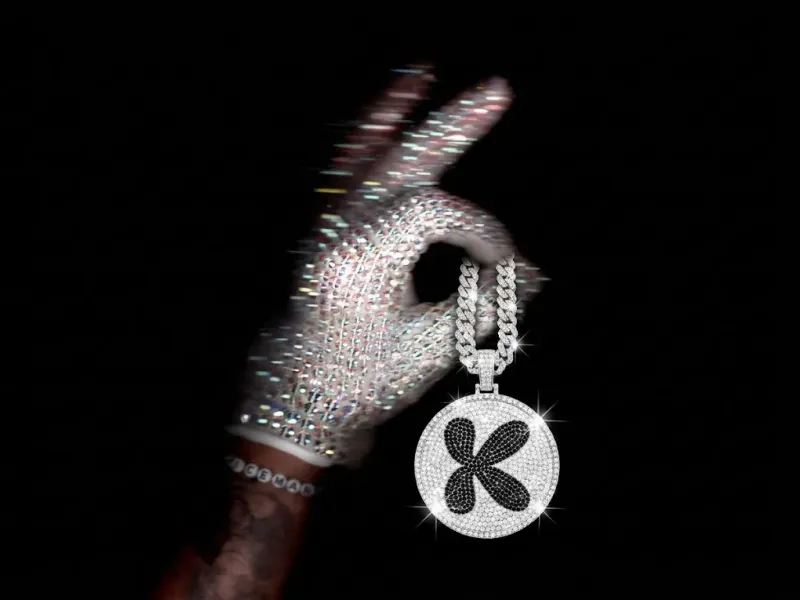 Round fully rhinestone-encrusted keychain with a rhinestone brand logo and a thick diamond chain threaded through the thumb of a sparkling crystal-gloved hand, white background, luxury product edit