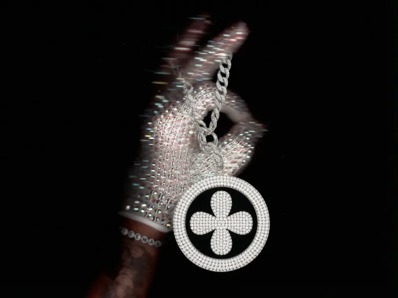 Round fully rhinestone-encrusted keychain with a rhinestone brand logo and a thick diamond chain threaded through the thumb of a sparkling crystal-gloved hand, white background, luxury product edit