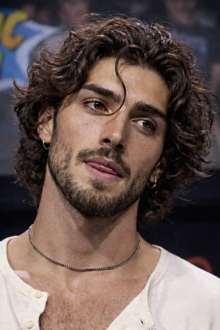Headshot reference of a young man with dark curly hair, beard, hoop earring, and a beige henley shirt — used as identity anchor for the private-jet portrait edit