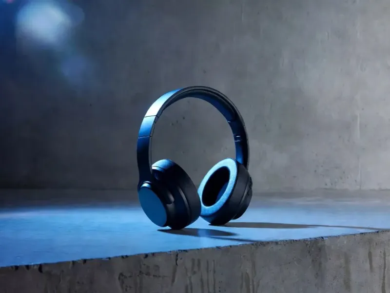 Wireless headphones resting on a minimalist concrete surface under moody blue-tinted studio lighting with a subtle lens flare, low-angle premium product shot