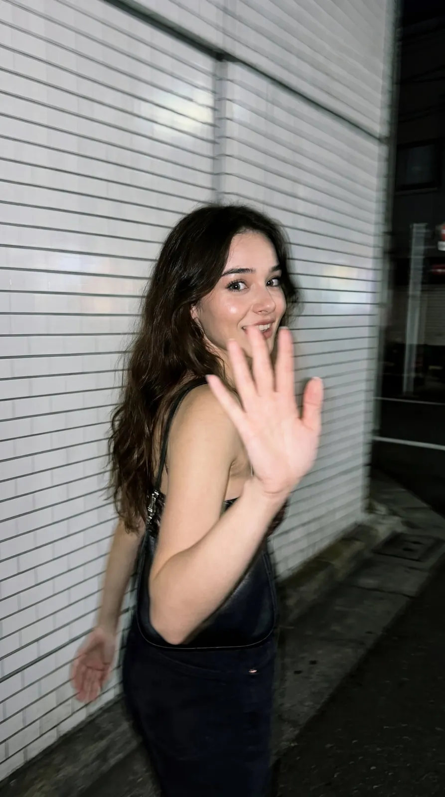 Ultra-realistic candid smartphone flash photo at night in Tokyo, subject mid-walk with raised hand blocking camera and motion-blurred face against white ceramic tile wall